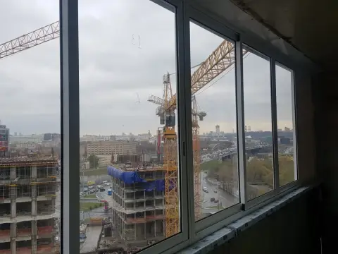 Алюминиевое остекление с раздвижными створками, балкон без внутренней отделки, вид на стройку с кранами