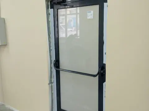 Дверь со стеклом и горизонтальной ручкой в тёмно-сером профиле, проём в бежевой стене